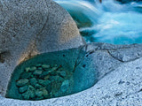 small pool in granite rock with river in background small pool in granite rock with river in background