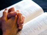 folded hands on an open bible in devotion